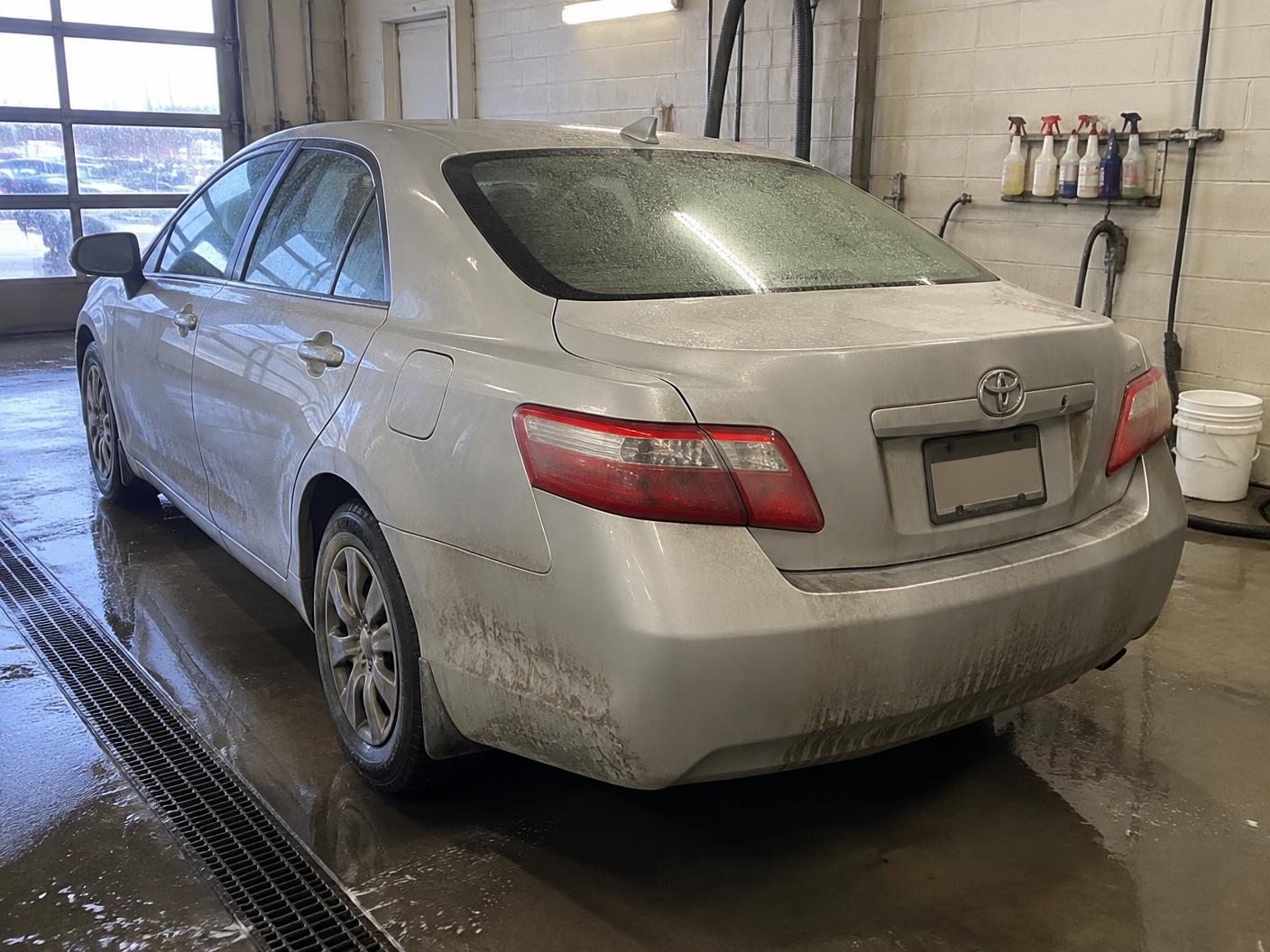 Silver sedan before exterior detailing with road film and dirt across the rear panels